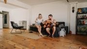 wood flooring man sitting and playing acoustic guitar near woman in living room