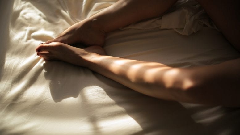 human feet on white bedspread close-up photography