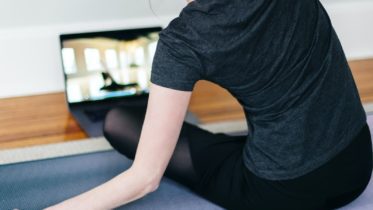 woman in black t-shirt and black pants lying on black yoga mat warm up
